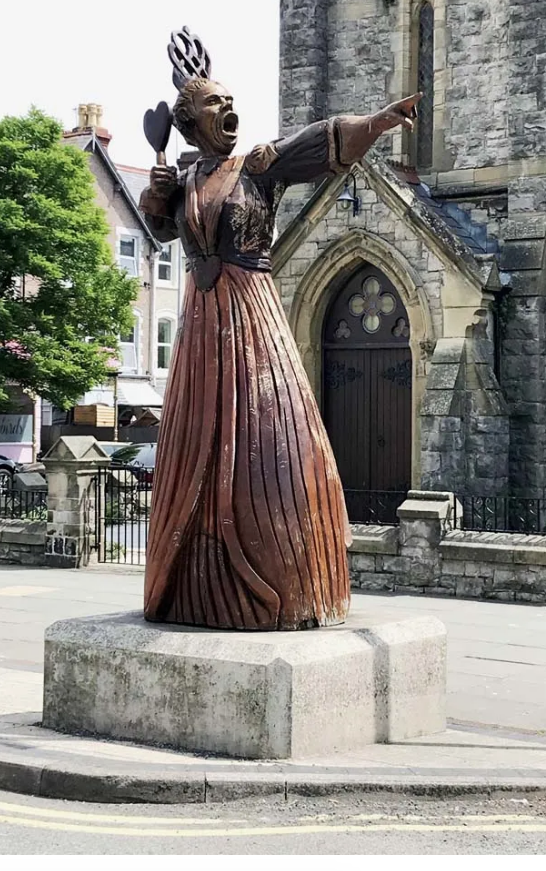A statue of a woman in a long dress is standing in front of a church.