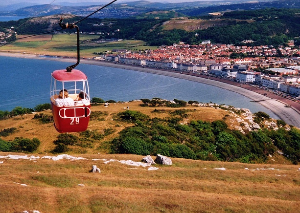 A red cable car is going up a hill overlooking the ocean