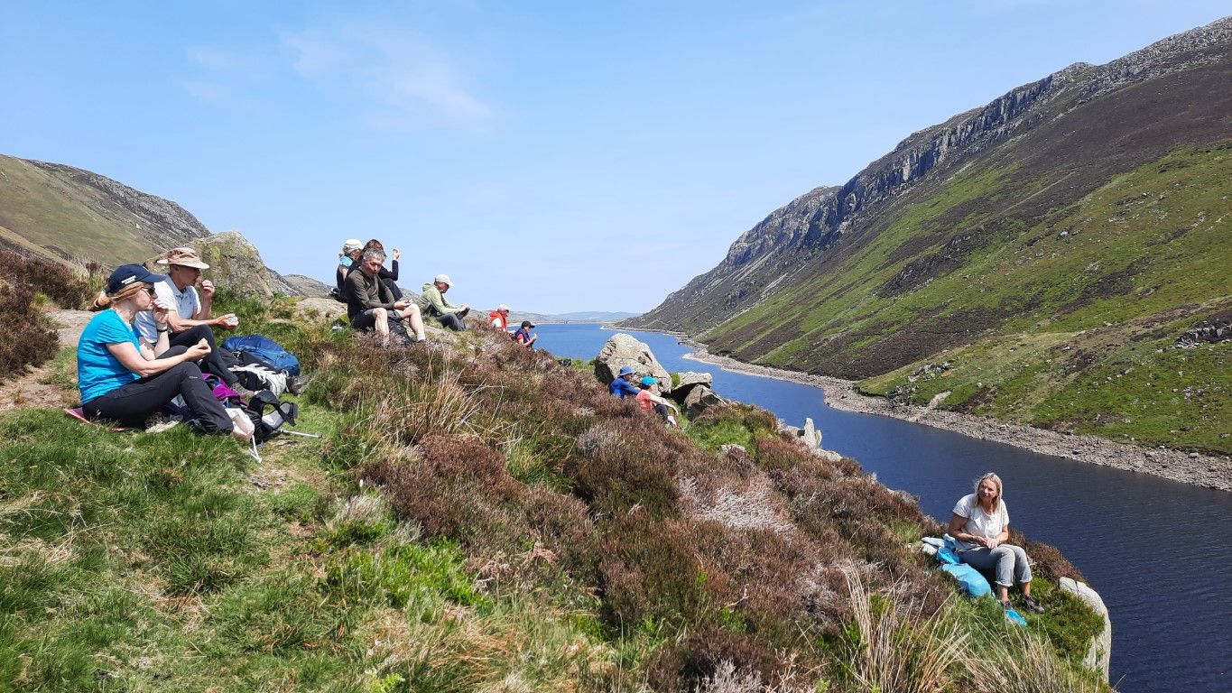 A group of people are sitting on top of a hill overlooking a river.