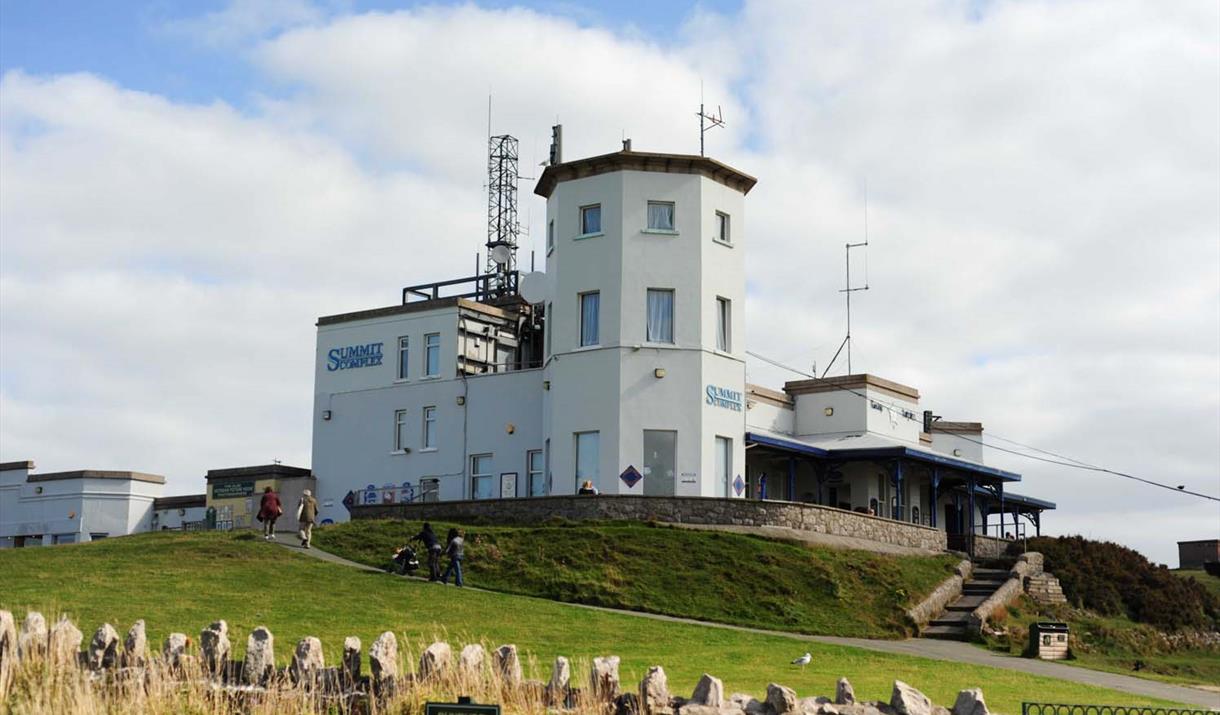 A large white building is sitting on top of a grassy hill.