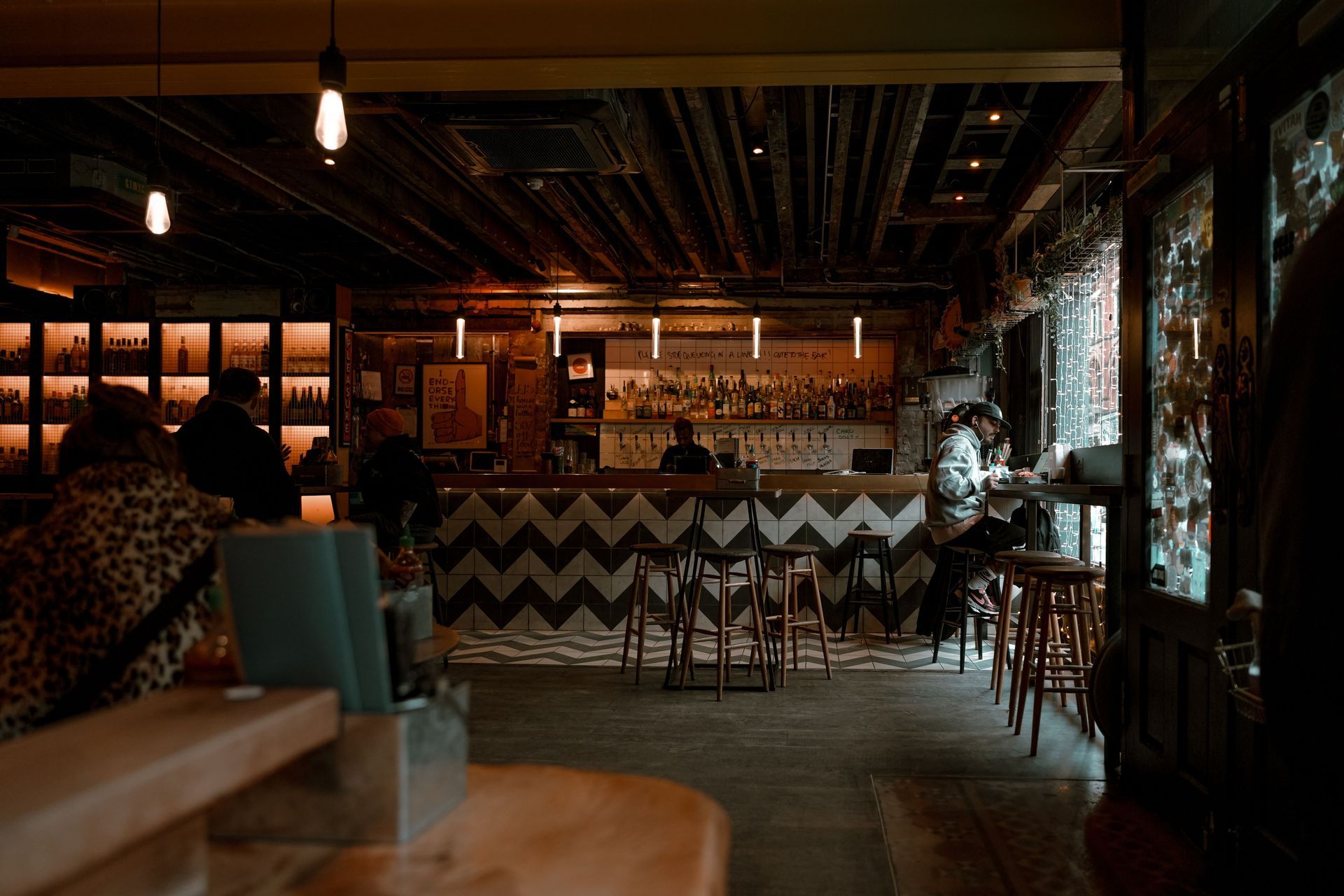 Dimly lit restaurant interior with a zigzag bar front, hanging lights, and patrons seated at tables
