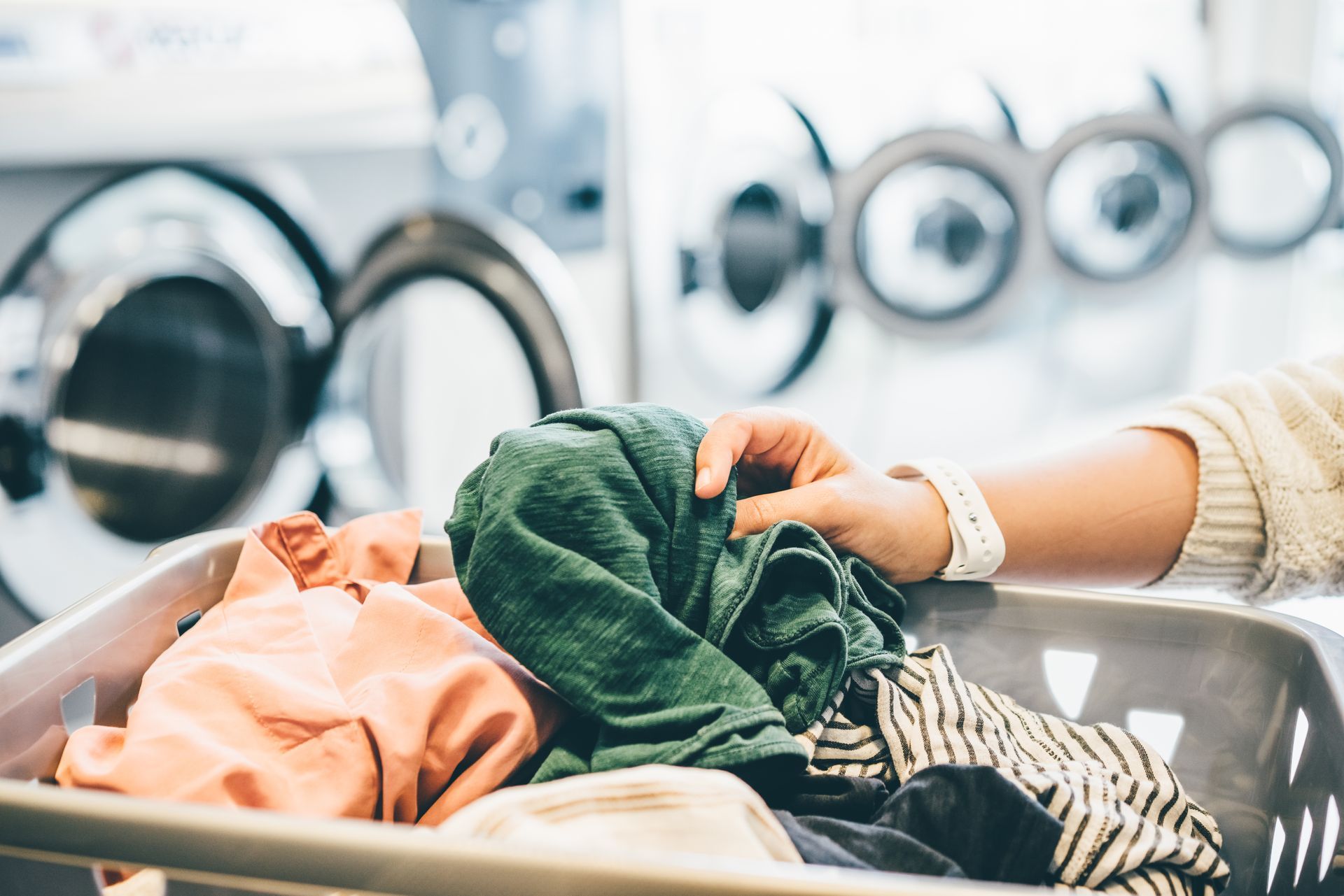 A person is putting clothes in a laundry basket in a laundromat.