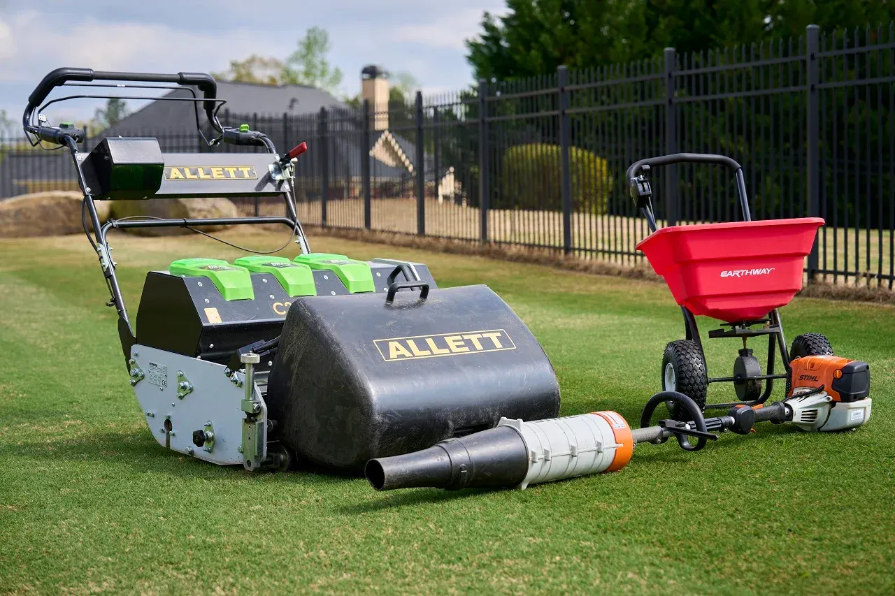 A lawn mower and a spreader are sitting on top of a lush green lawn.