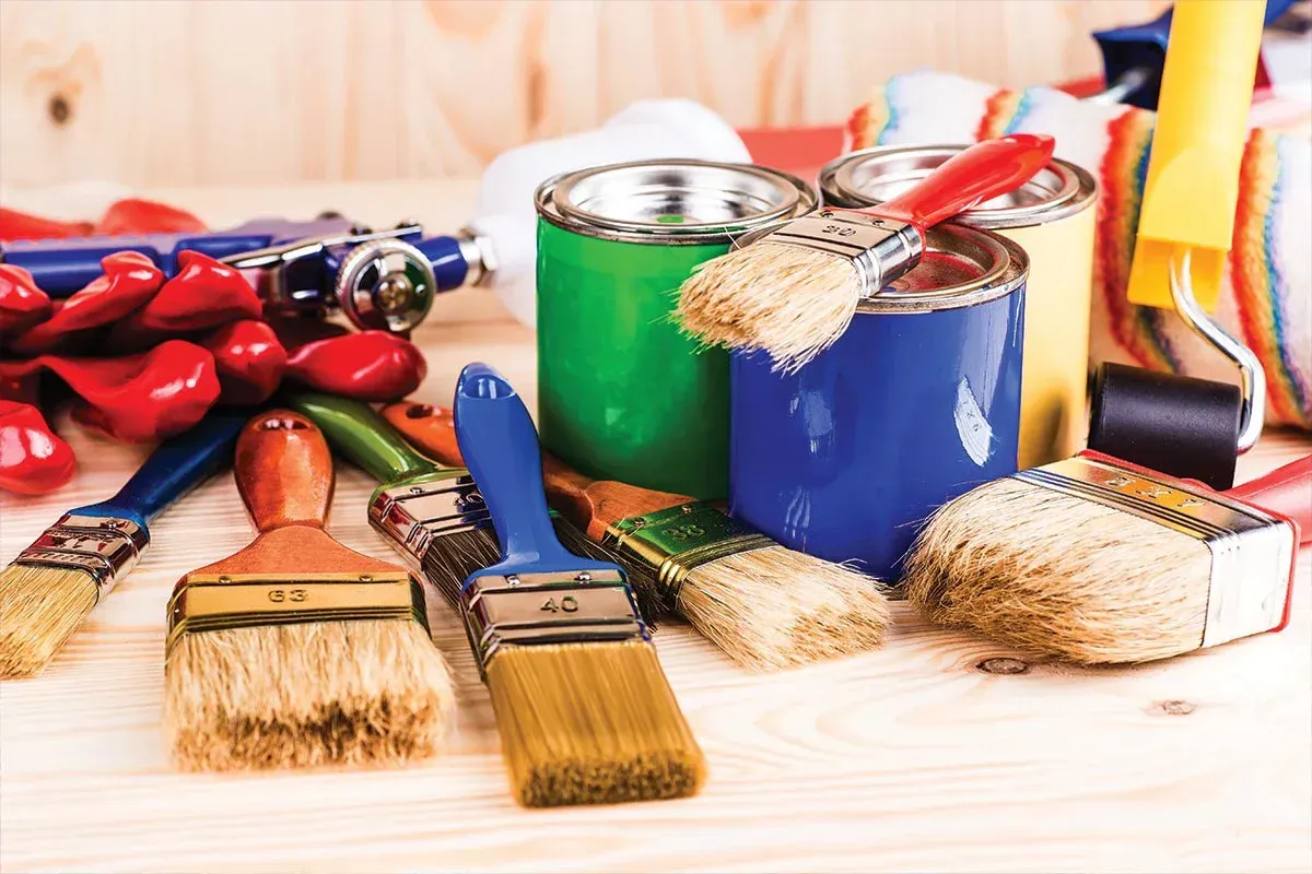 A bunch of paint brushes and cans of paint on a wooden table.