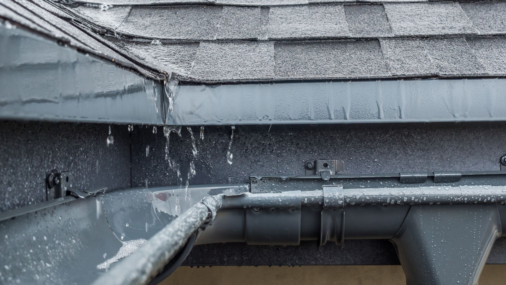 Water pouring off a gray shingled roof and gutter in the rain