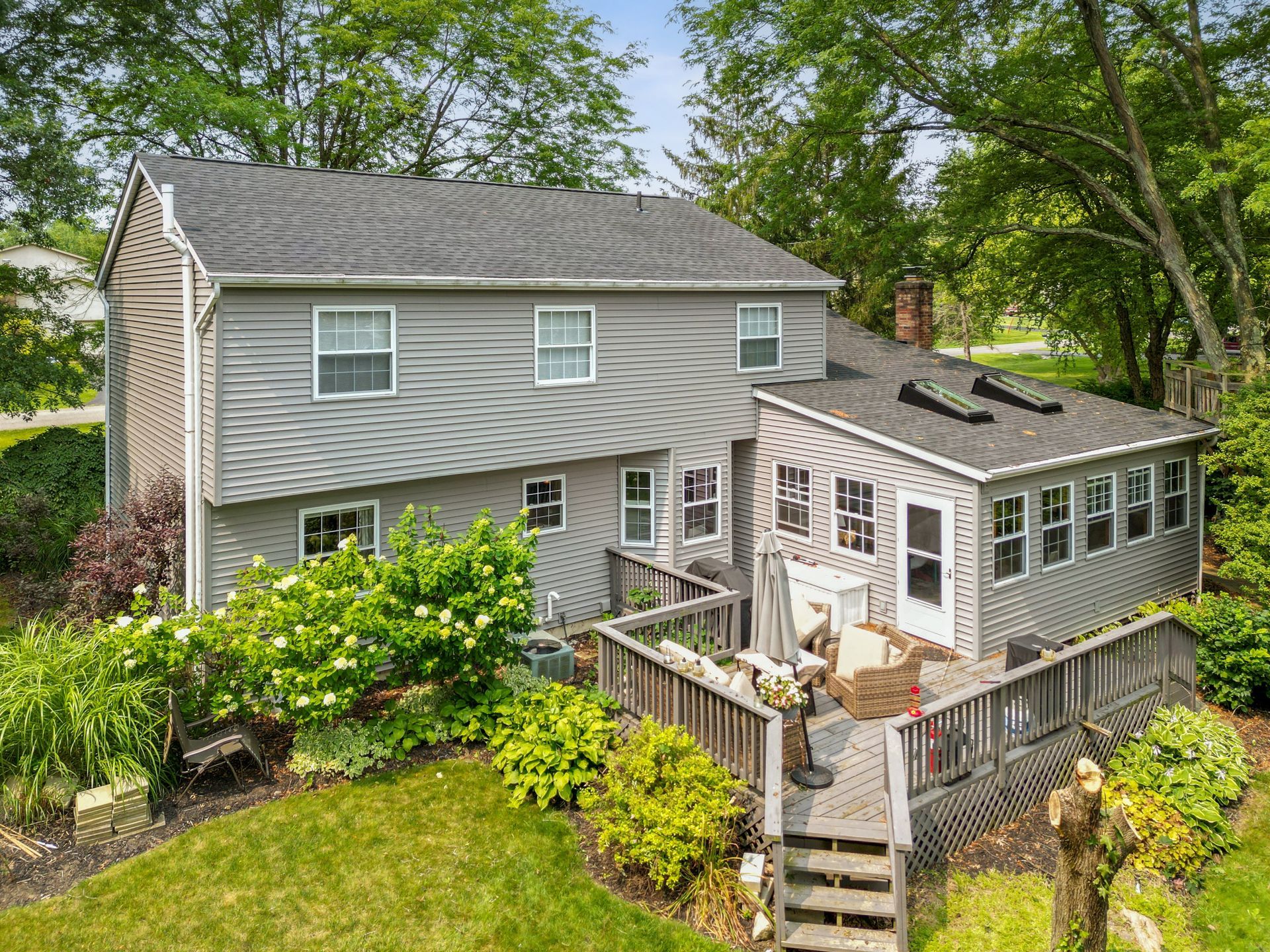 Gray two-story house with a deck and screened porch, surrounded by green trees and shrubs.