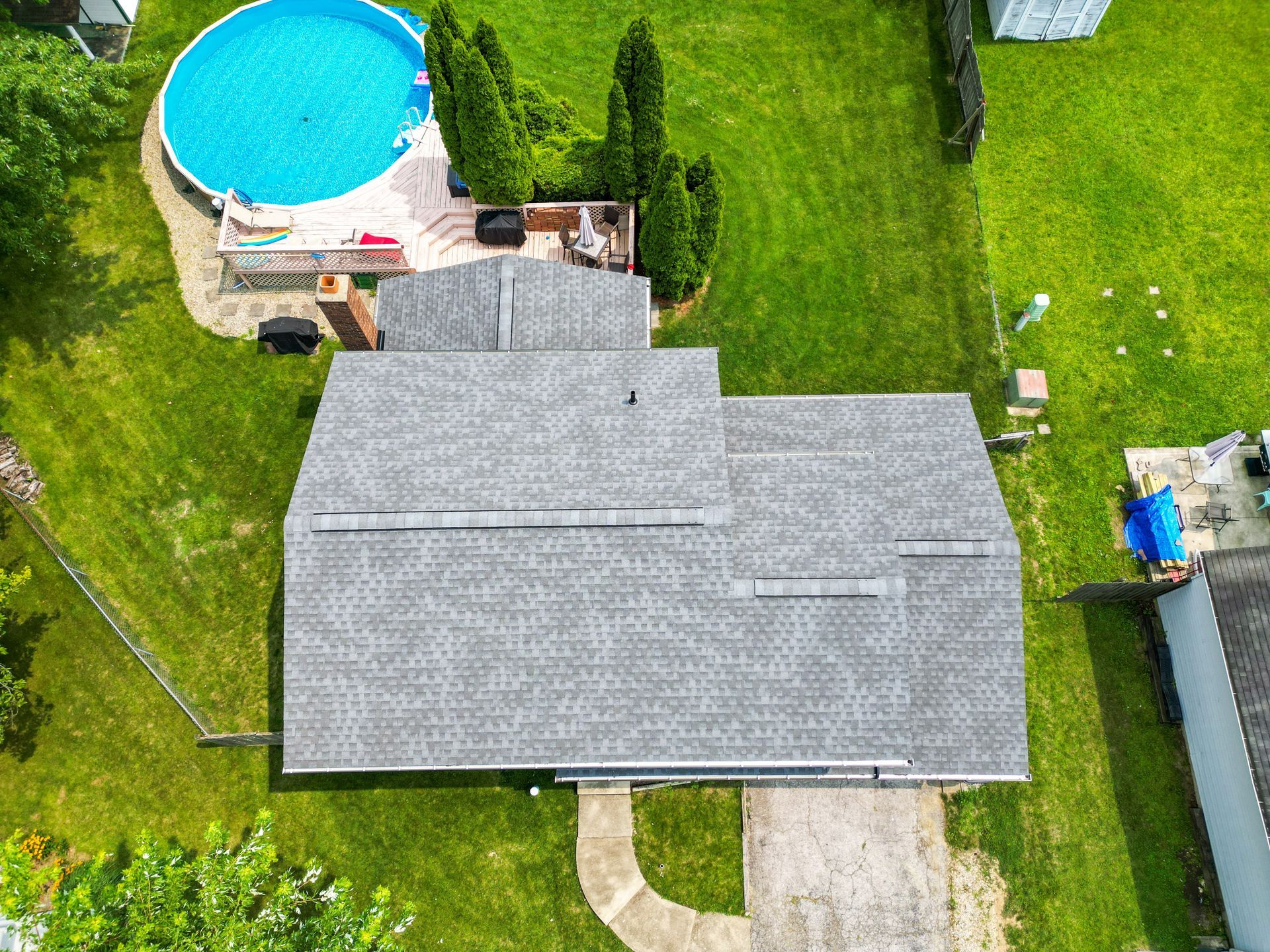 Aerial view of a house with a gray roof, green lawn, and an above-ground pool in the backyard.