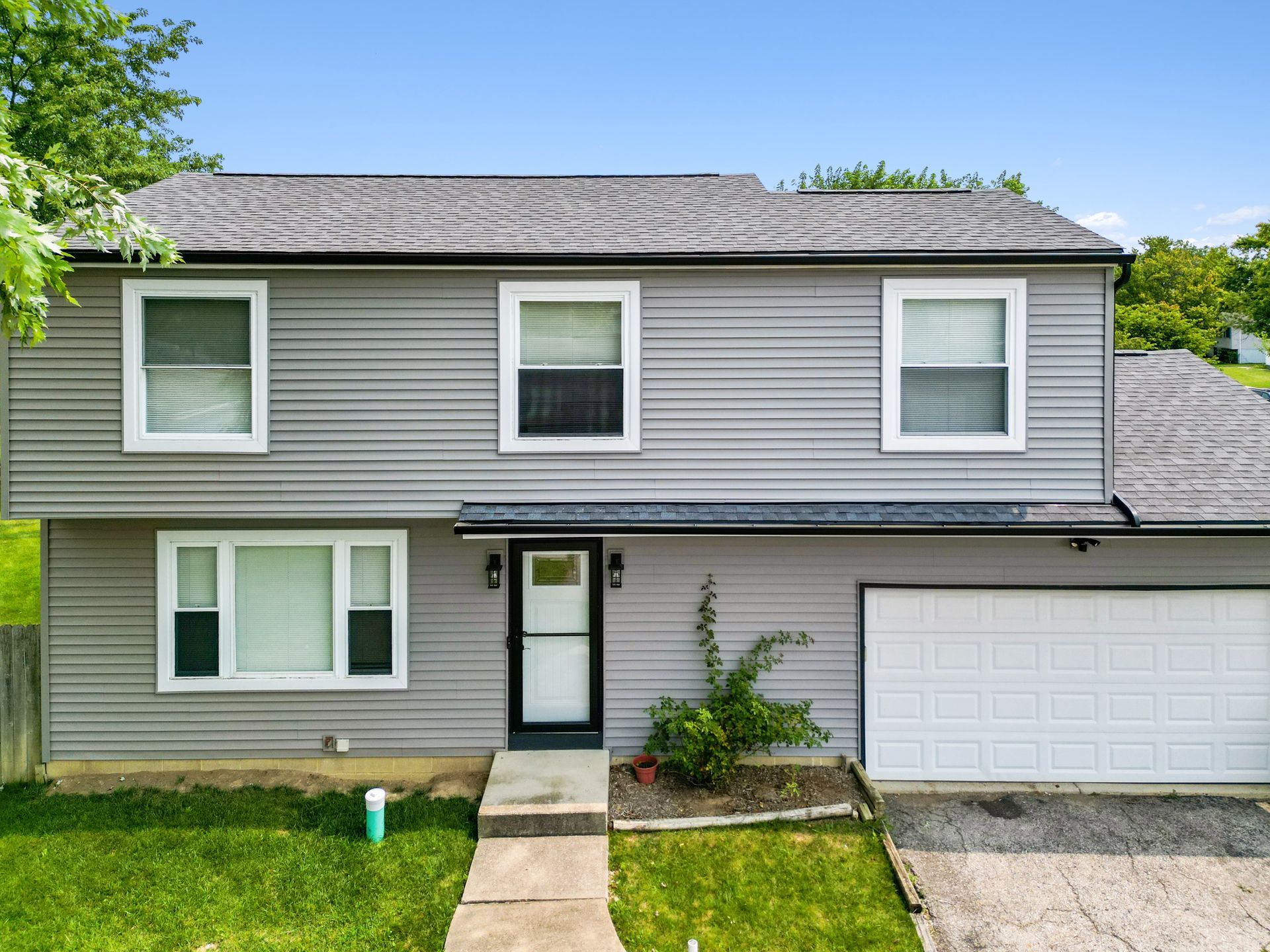 Two-story gray house with white trim, attached garage, and green lawn under a blue sky