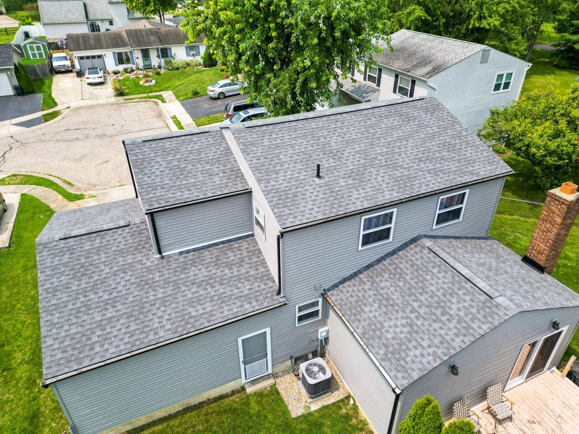 Aerial view of a gray two-story house with a detached garage and green yard in a suburban neighborhood