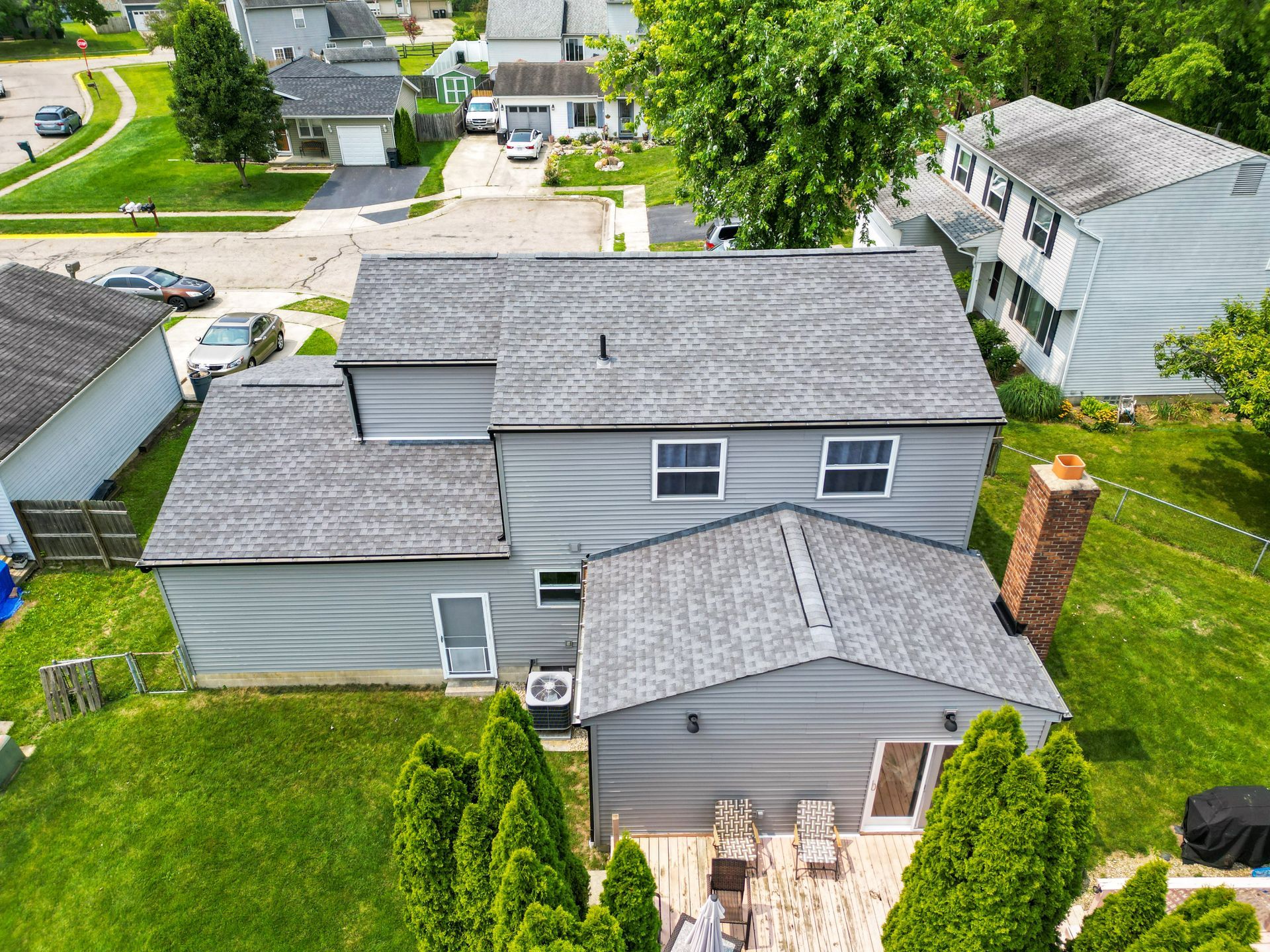 Aerial view of a gray suburban house with a green lawn and neighboring homes.