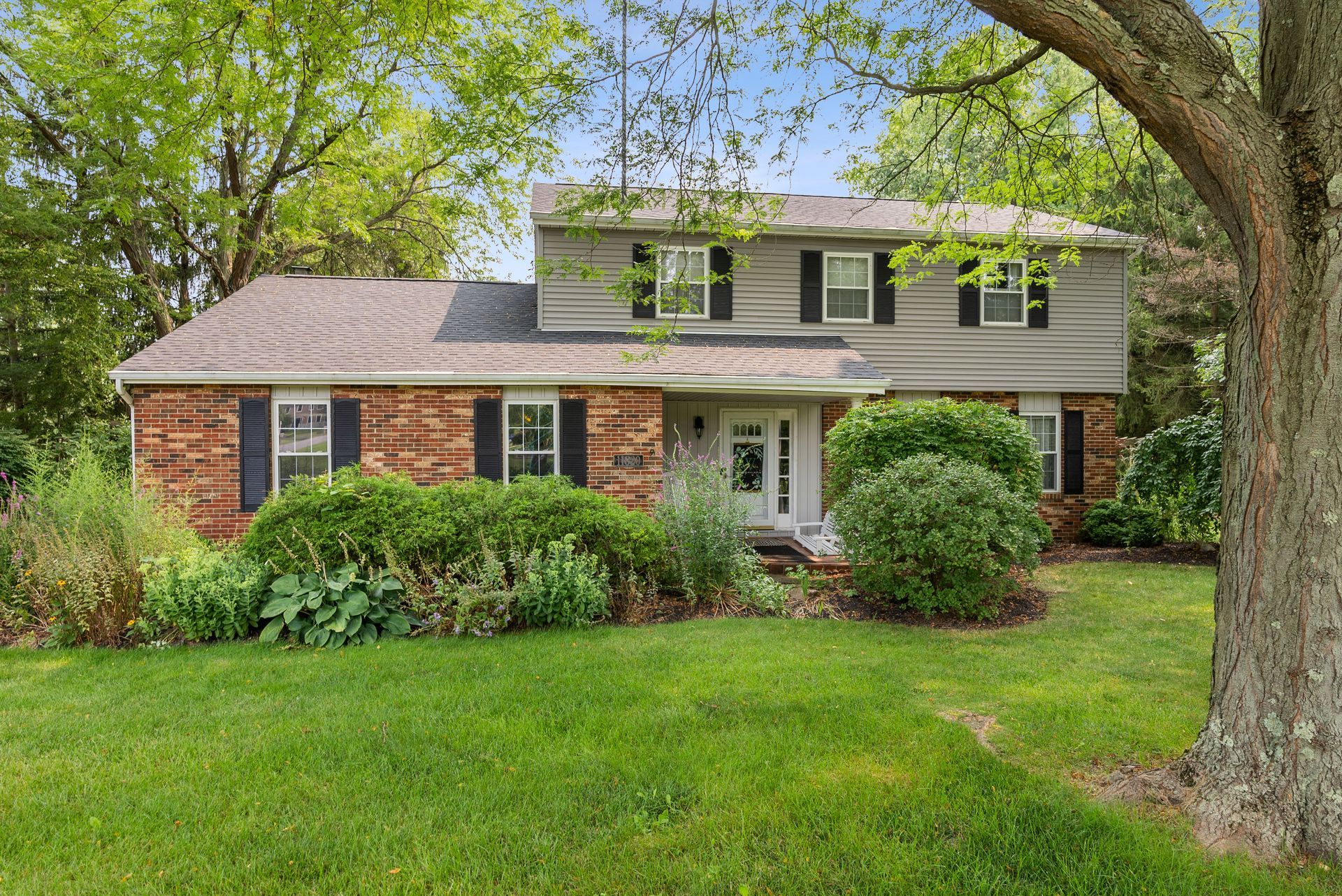 Brick-and-white two-story house with a lush green lawn and trees in front