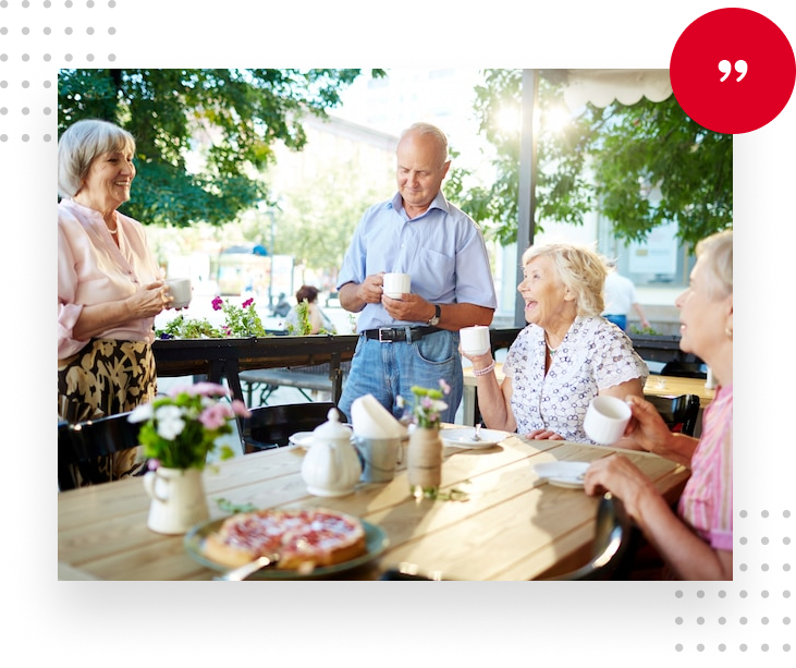 Friends chatting over coffee at an outdoor table in a sunny garden.