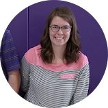 Smiling person with glasses and long hair wearing a striped shirt against a purple background