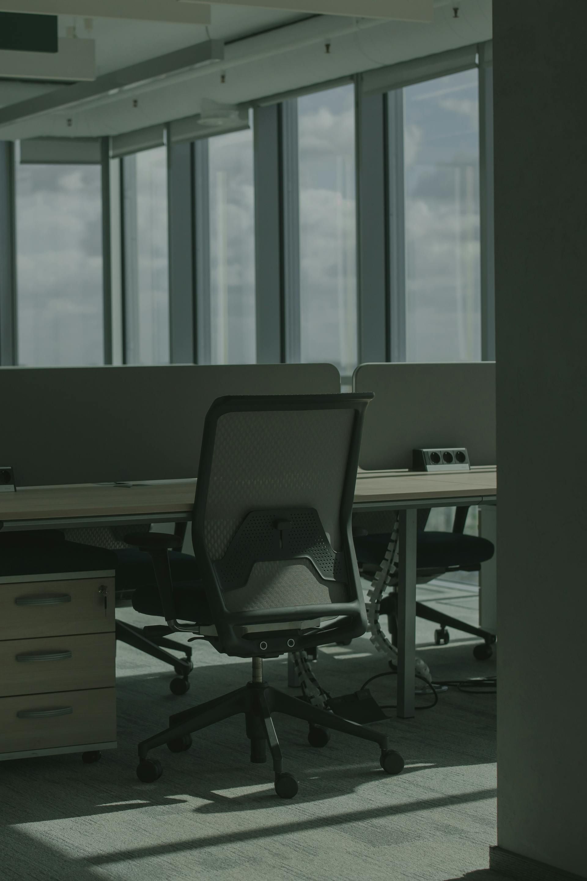 Office workspace with empty desk and ergonomic chair near large windows.