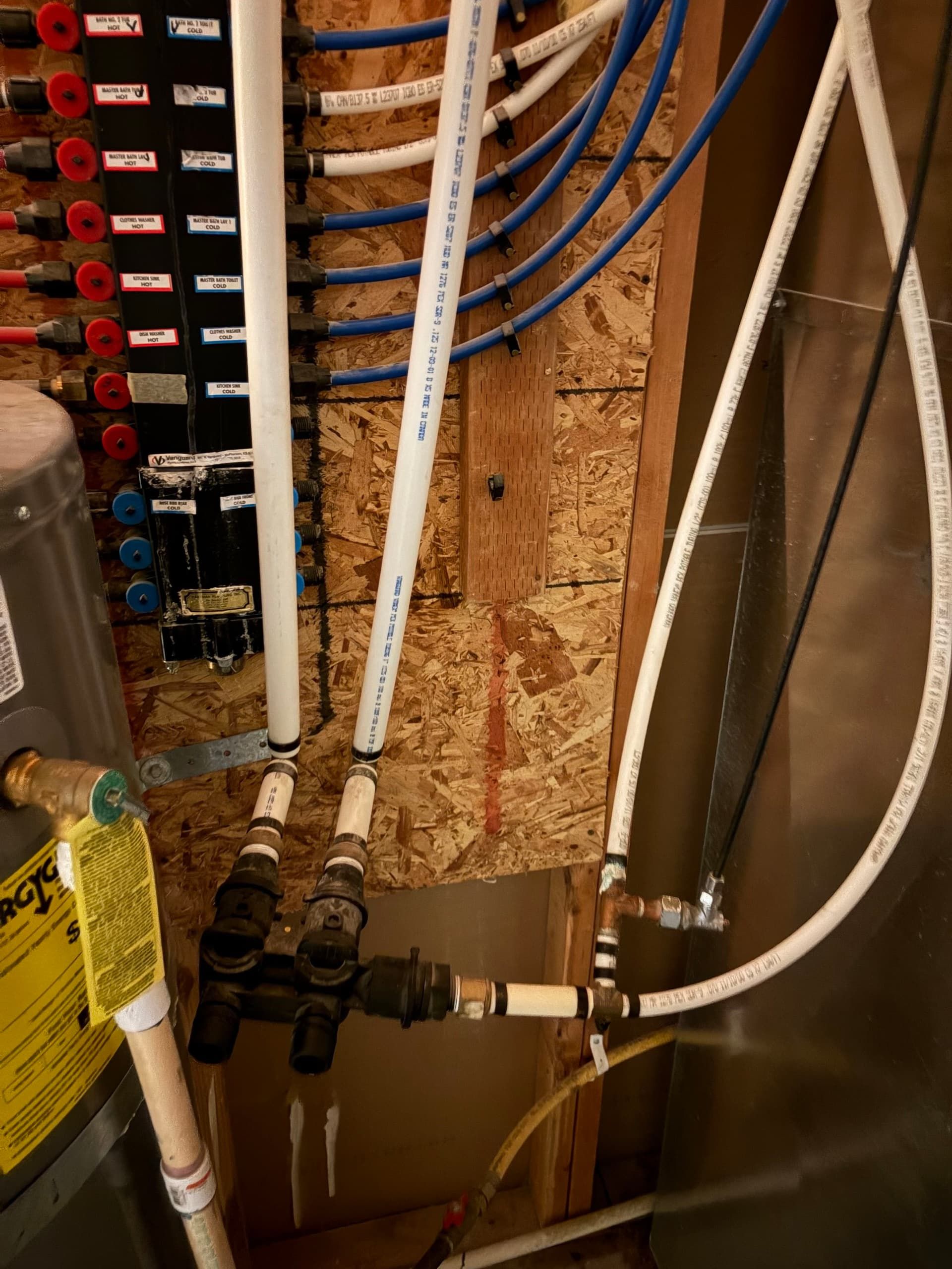 Close-up of plumbing pipes, valves, and blue hoses mounted on a wooden utility wall.