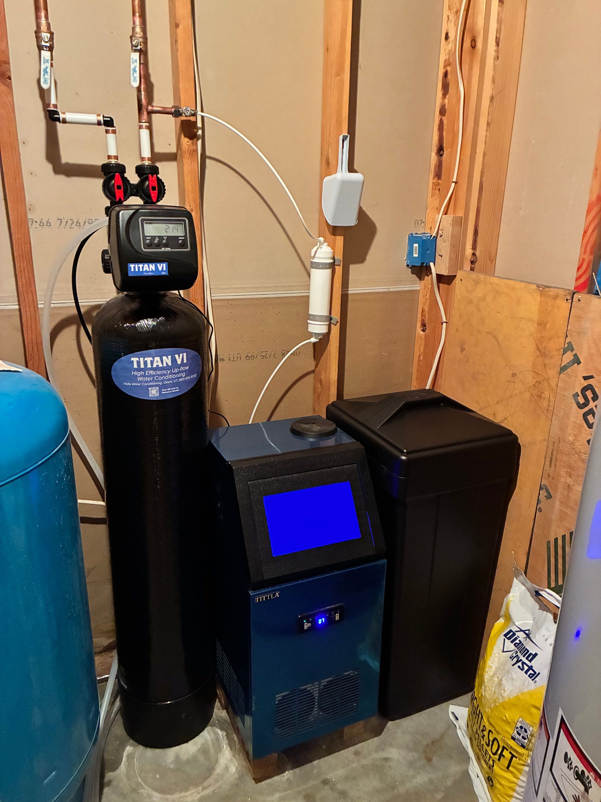 Water softener and filtration equipment in a utility room beside exposed pipes.