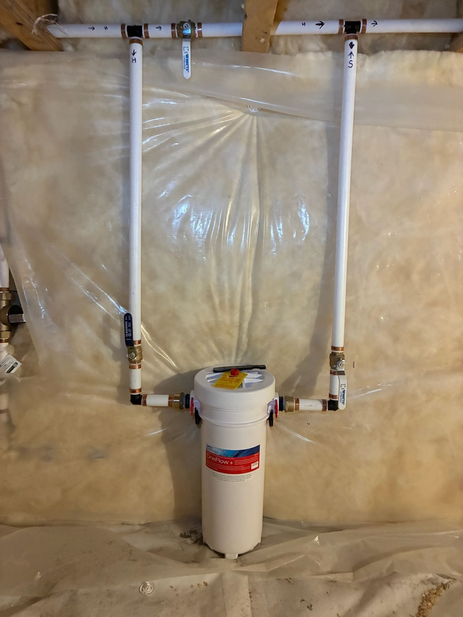 Basement wall with insulated plumbing pipes, white vertical pipe, and clear plastic vapor barrier.