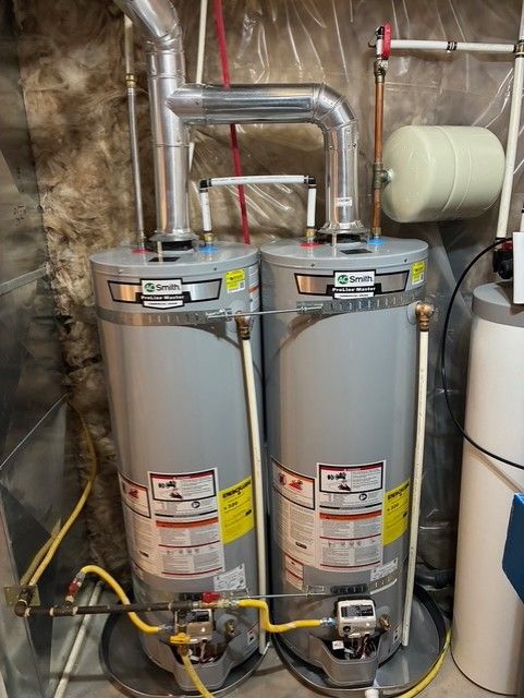 Two silver water heaters with pipes and valves in a utility room