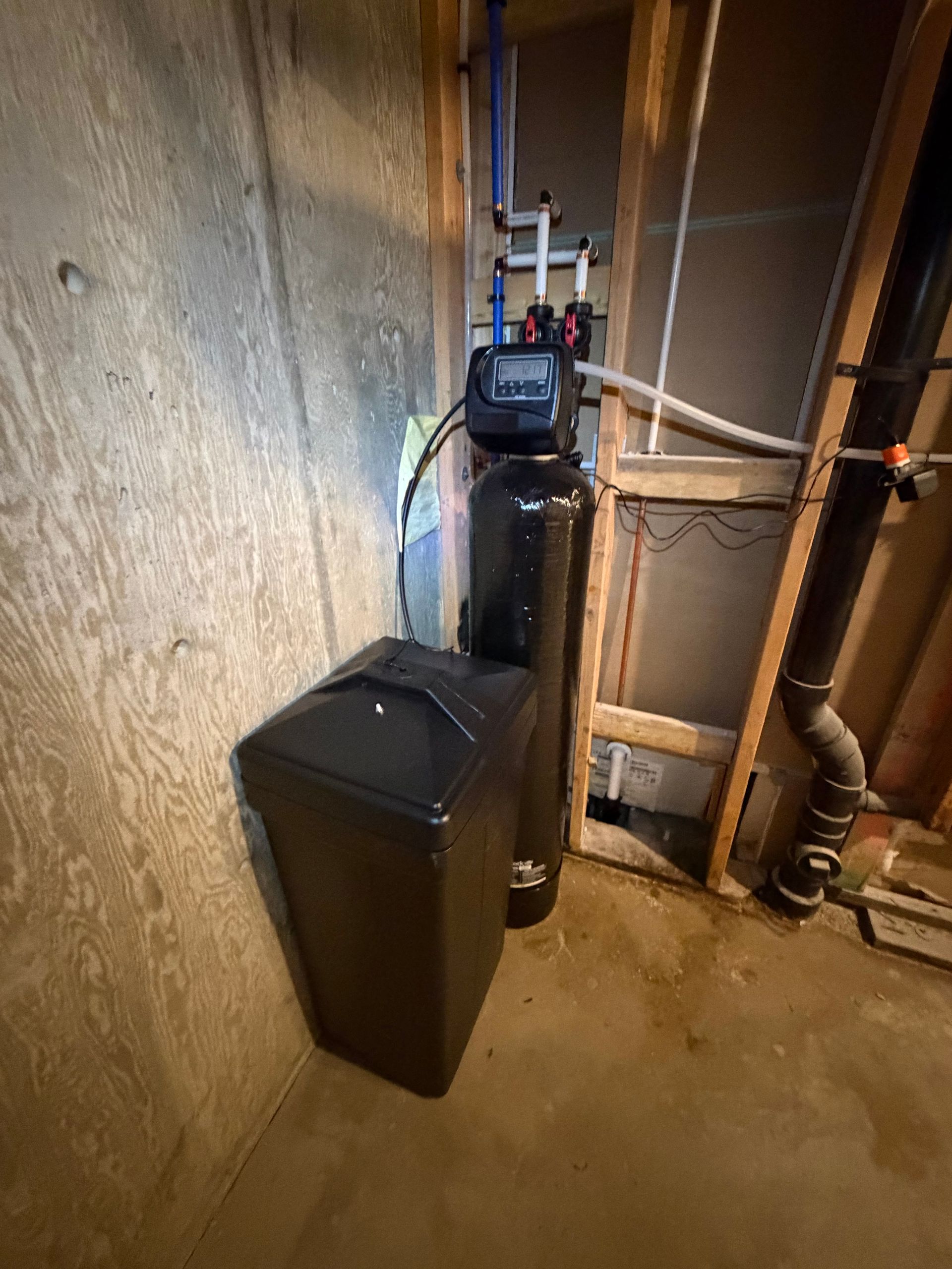 Water softener and plumbing equipment in a utility room with unfinished walls and concrete floor