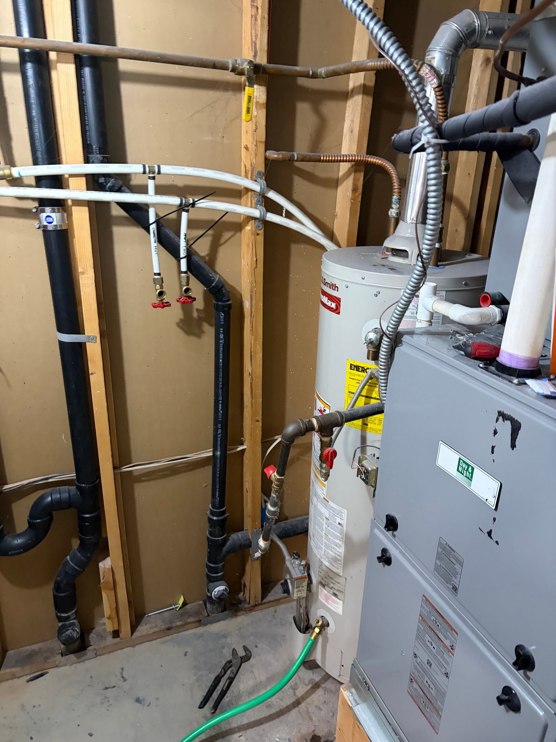 Utility room with exposed pipes, ducts, and two gray water heaters against unfinished wall studs.