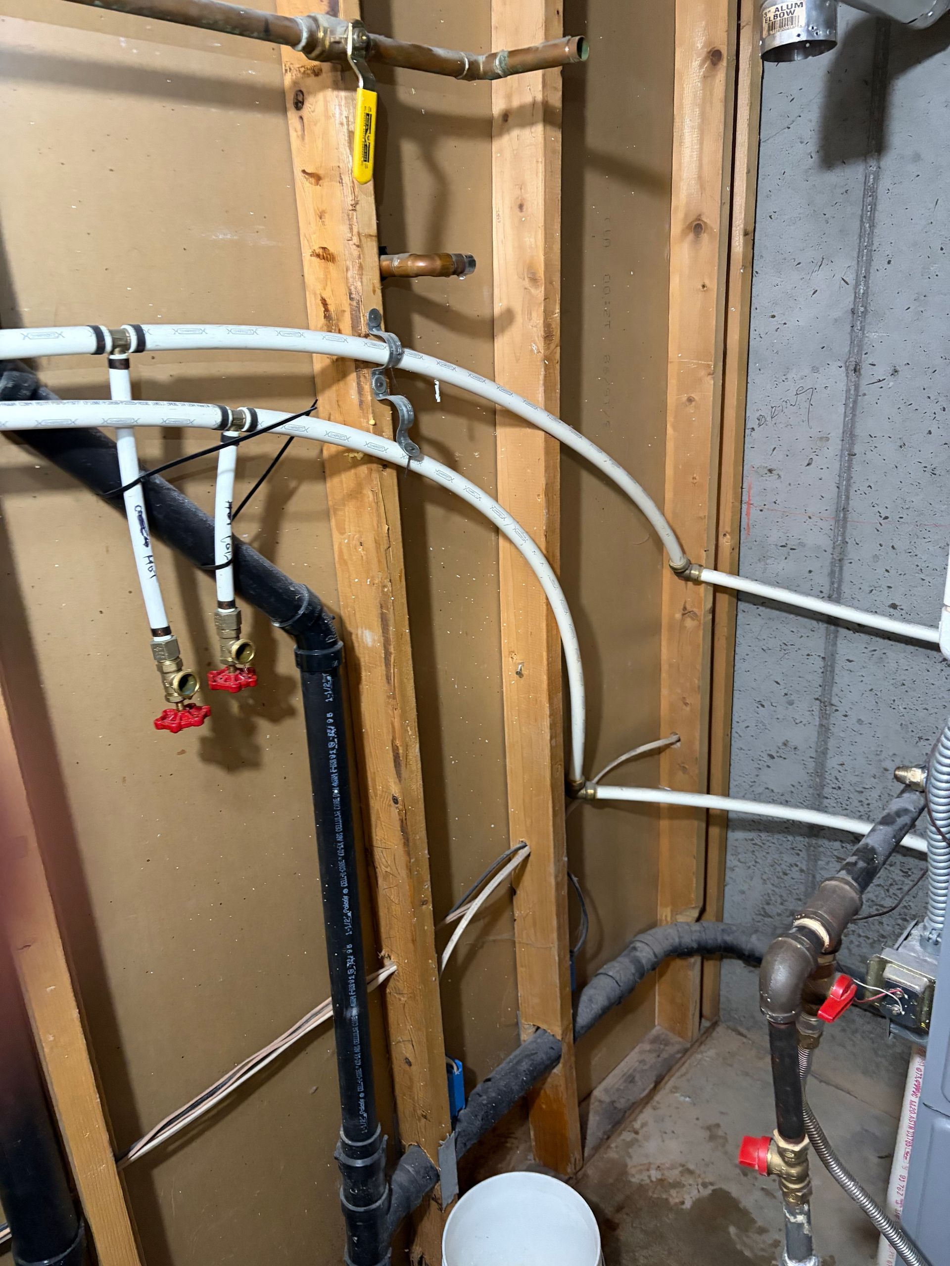 Exposed plumbing and pipes in a utility wall cavity with valves and wooden studs