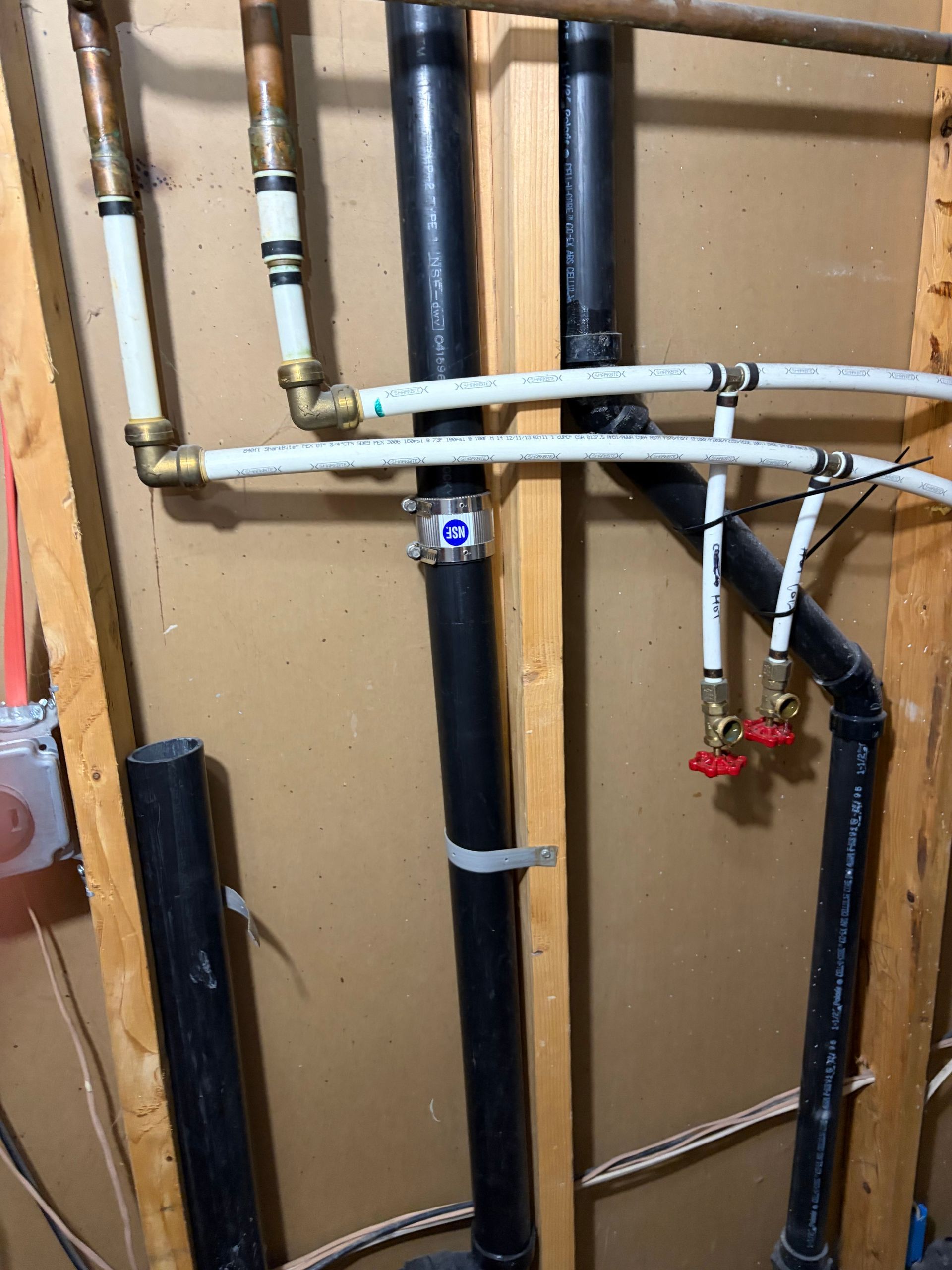Utility pipes and valves on a wooden wall, including black, copper, and white plumbing lines.