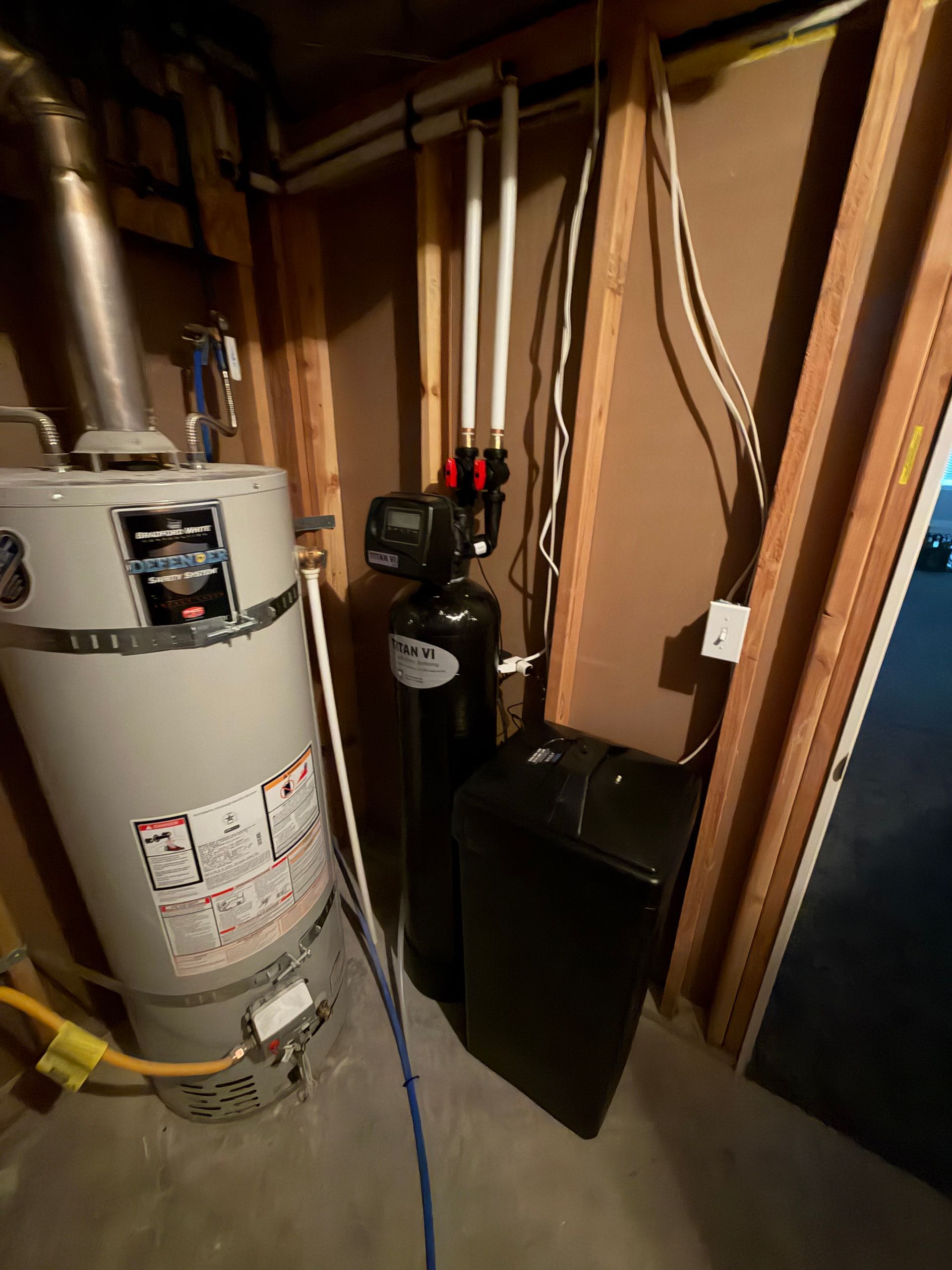 Utility closet with water heater, furnace, and exposed pipes in a cramped basement space