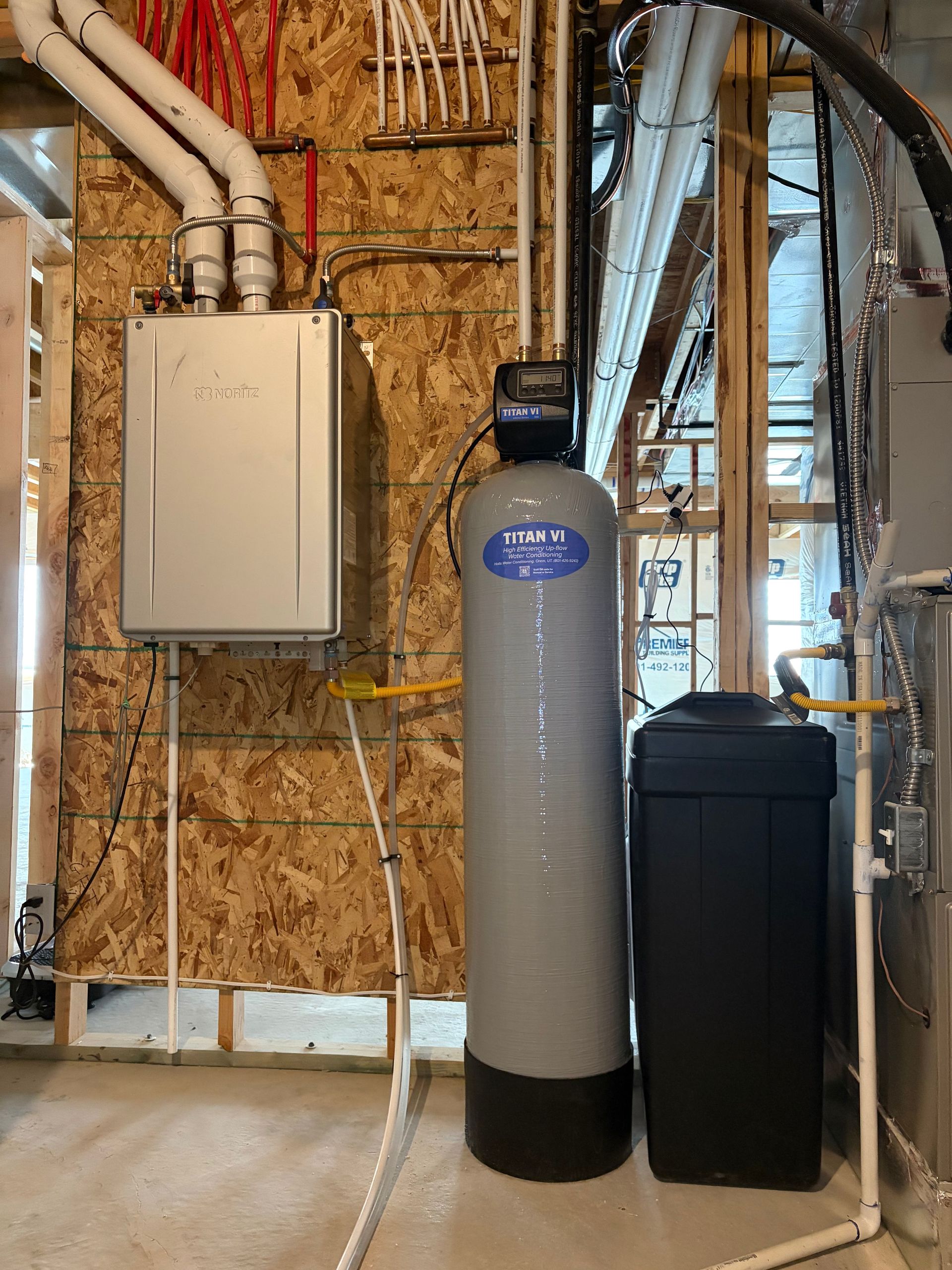 Basement utility area with furnace, water softener tank, and black storage bin against unfinished wood framing