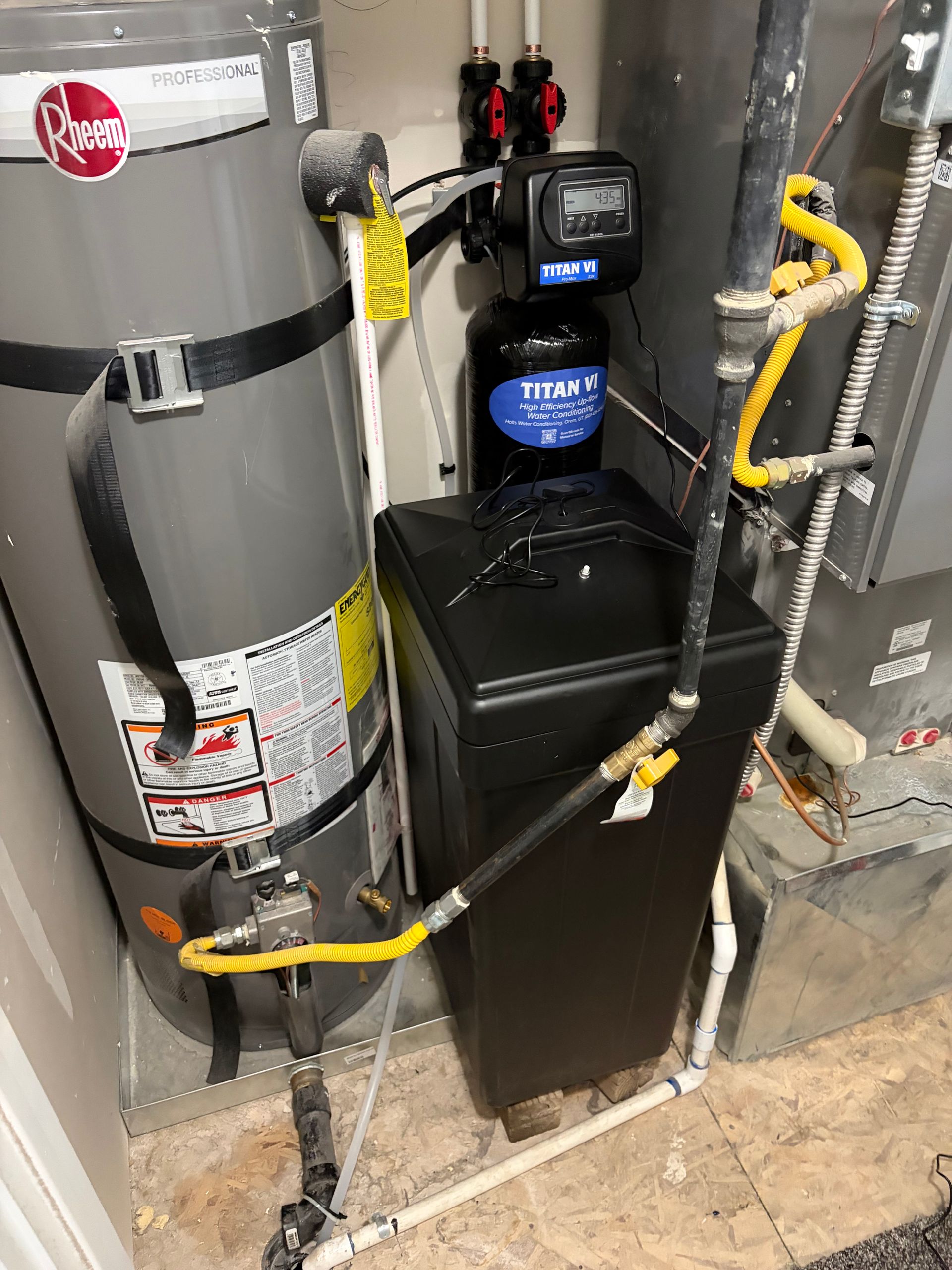 Water softener and filtration tanks with hoses and control units in a utility room.