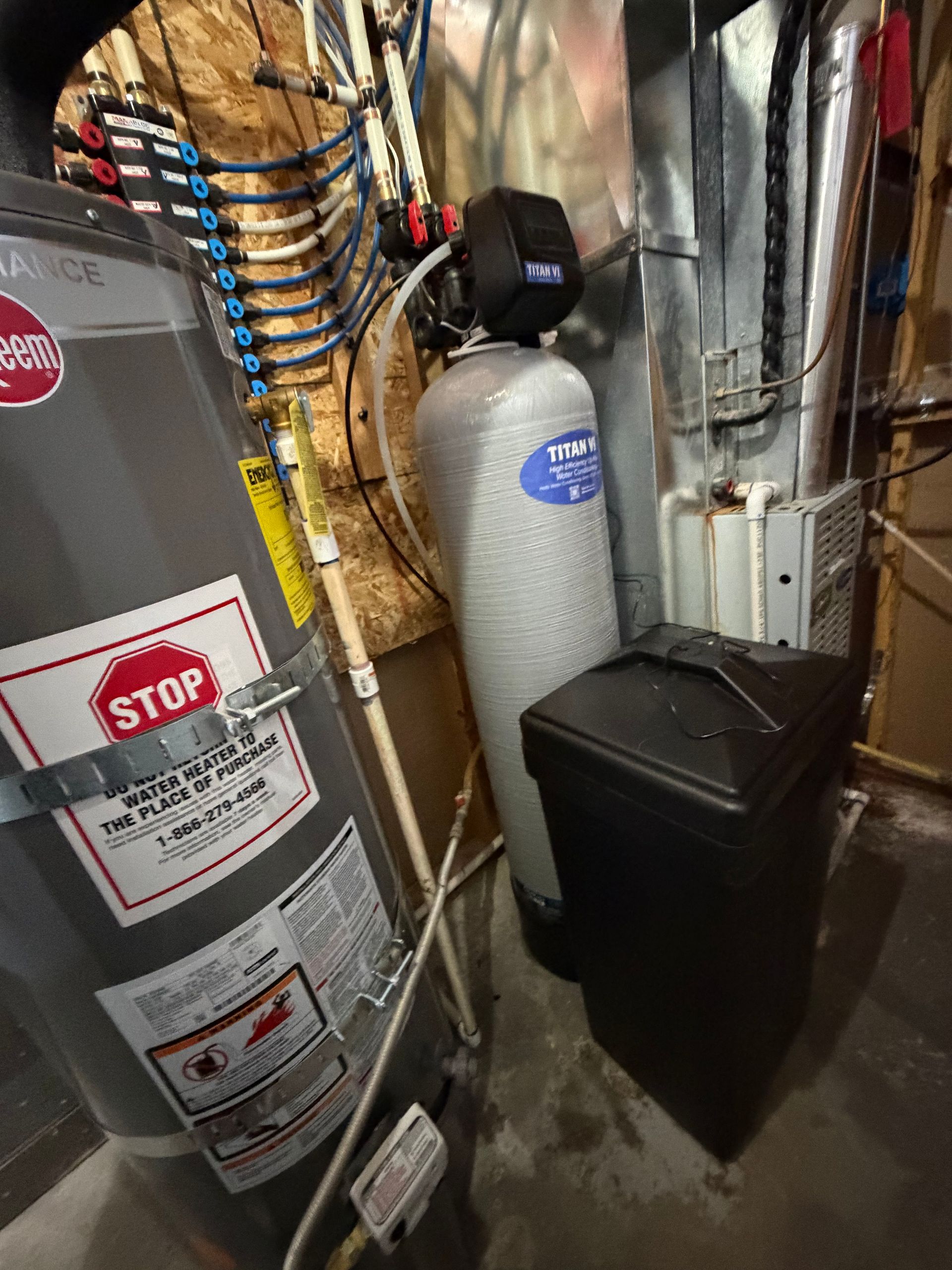 Basement utility room with water softener tank, furnace, pipes, and a black storage bin