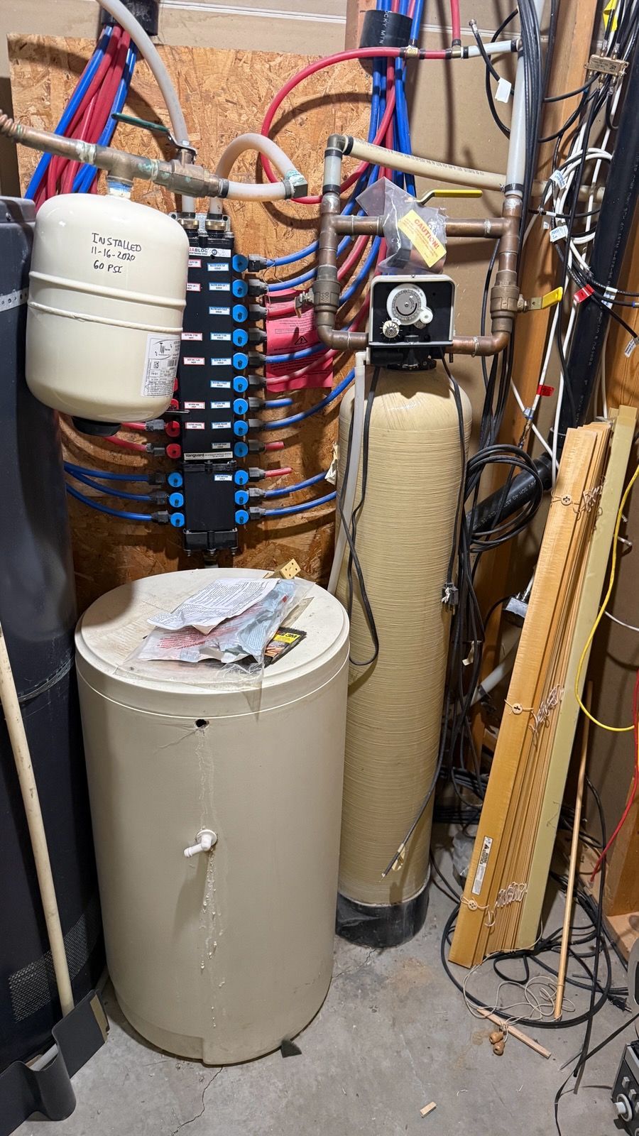 Utility room with water heaters, pipes, and plumbing equipment crowded in a basement corner