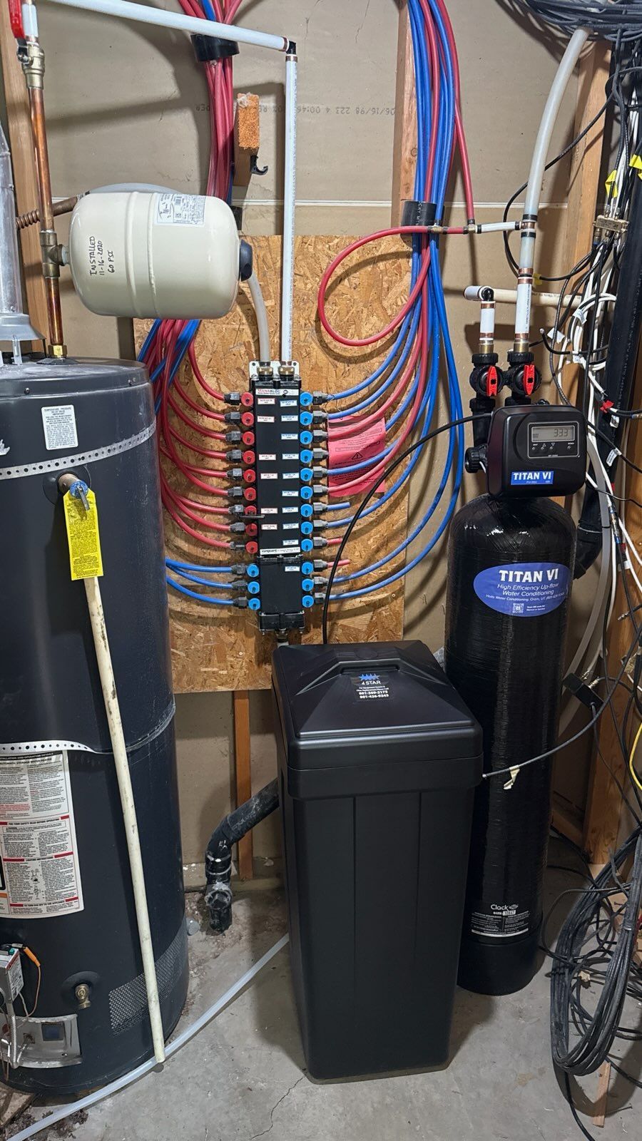Basement utility room with plumbing pipes, water heater tank, electrical wiring, and a black filtration tank.