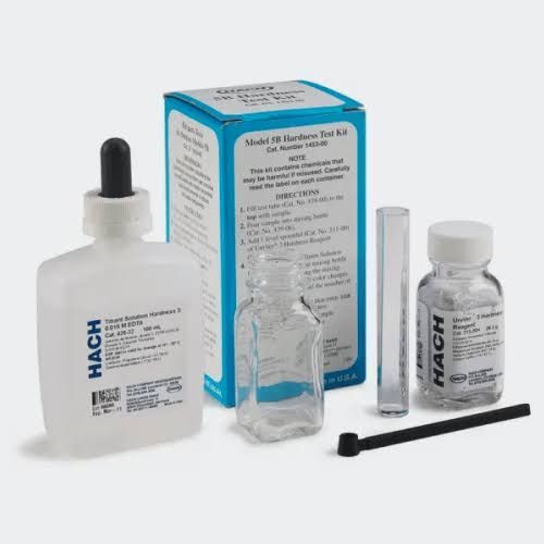 Hand dipping a test strip into a glass of water beside a pH test tube and color chart
