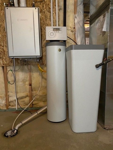 Basement utility area with furnace, water heater, and filtration tank beside exposed pipes and insulation