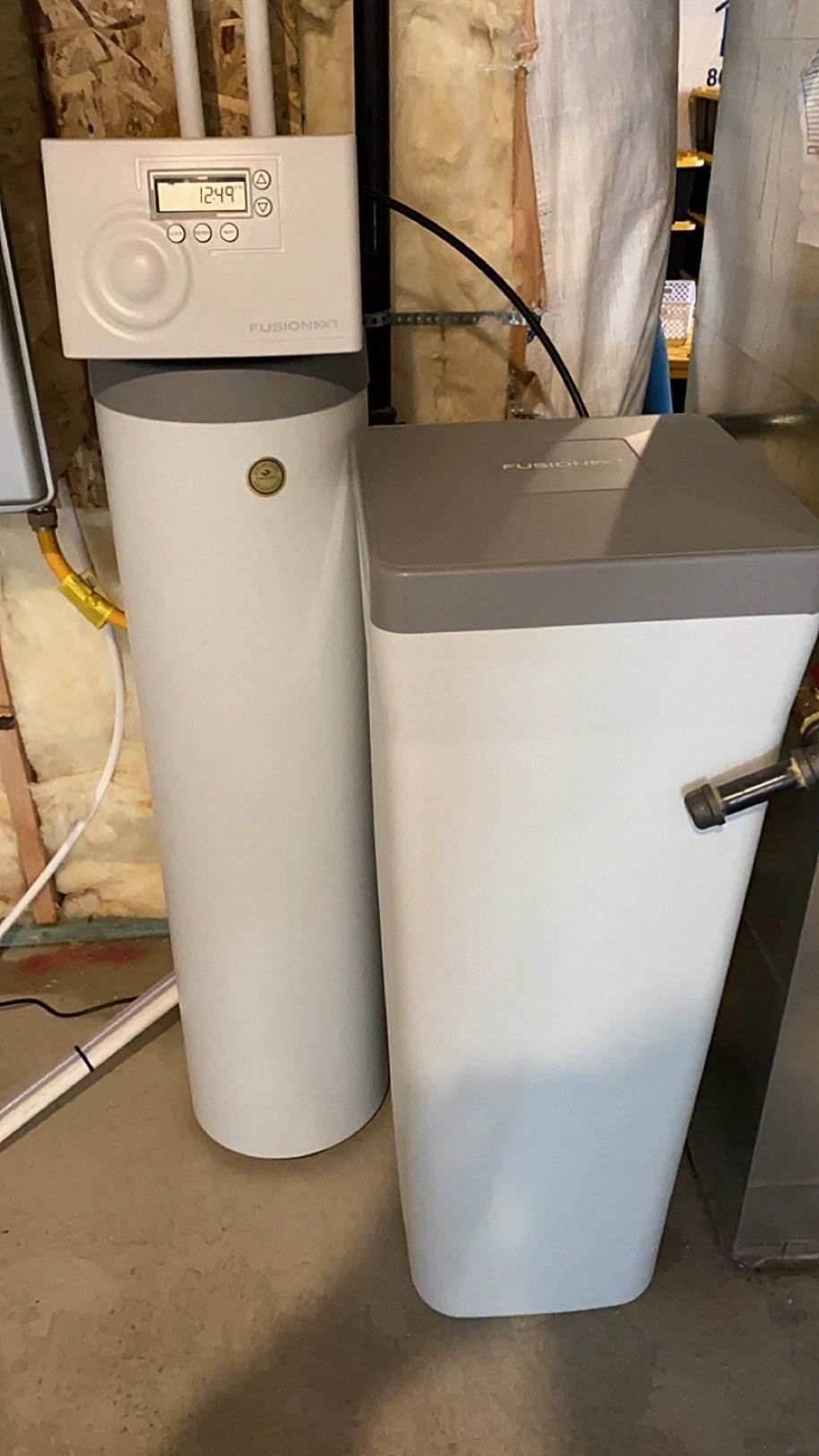 Two white water treatment tanks with a control panel in a basement utility area