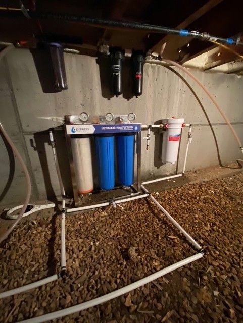 Under-sink water filter system with blue and white cartridges and visible pipes in a utility area
