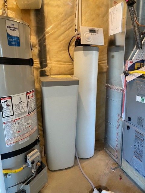Utility room with water heater, furnace, and insulated pipes in a basement corner