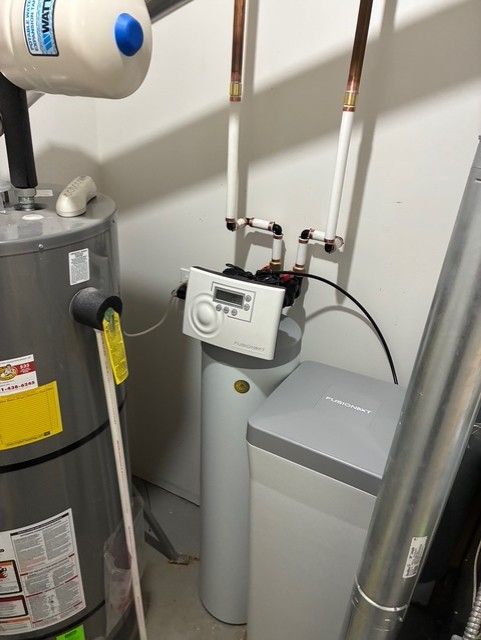 Water heater and water softener connected by copper pipes in a utility room.