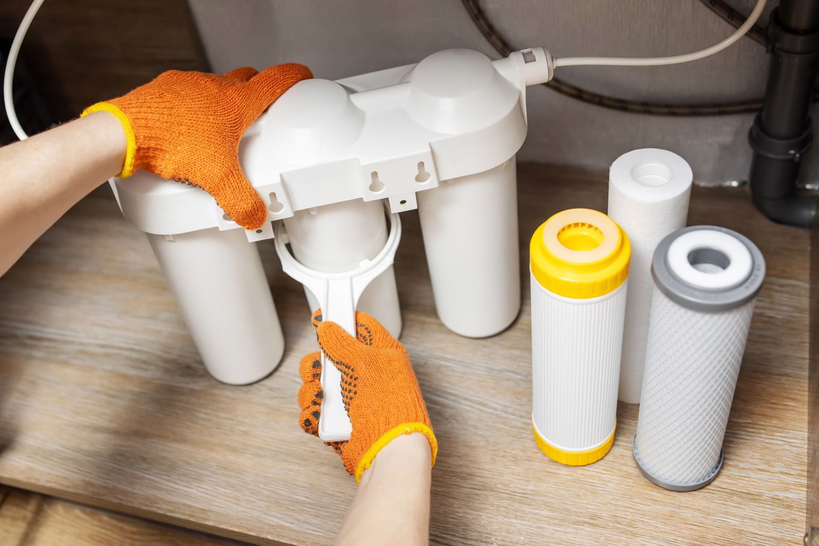 Hands replacing a water filter cartridge in a white under-sink filtration system, with spare filters nearby