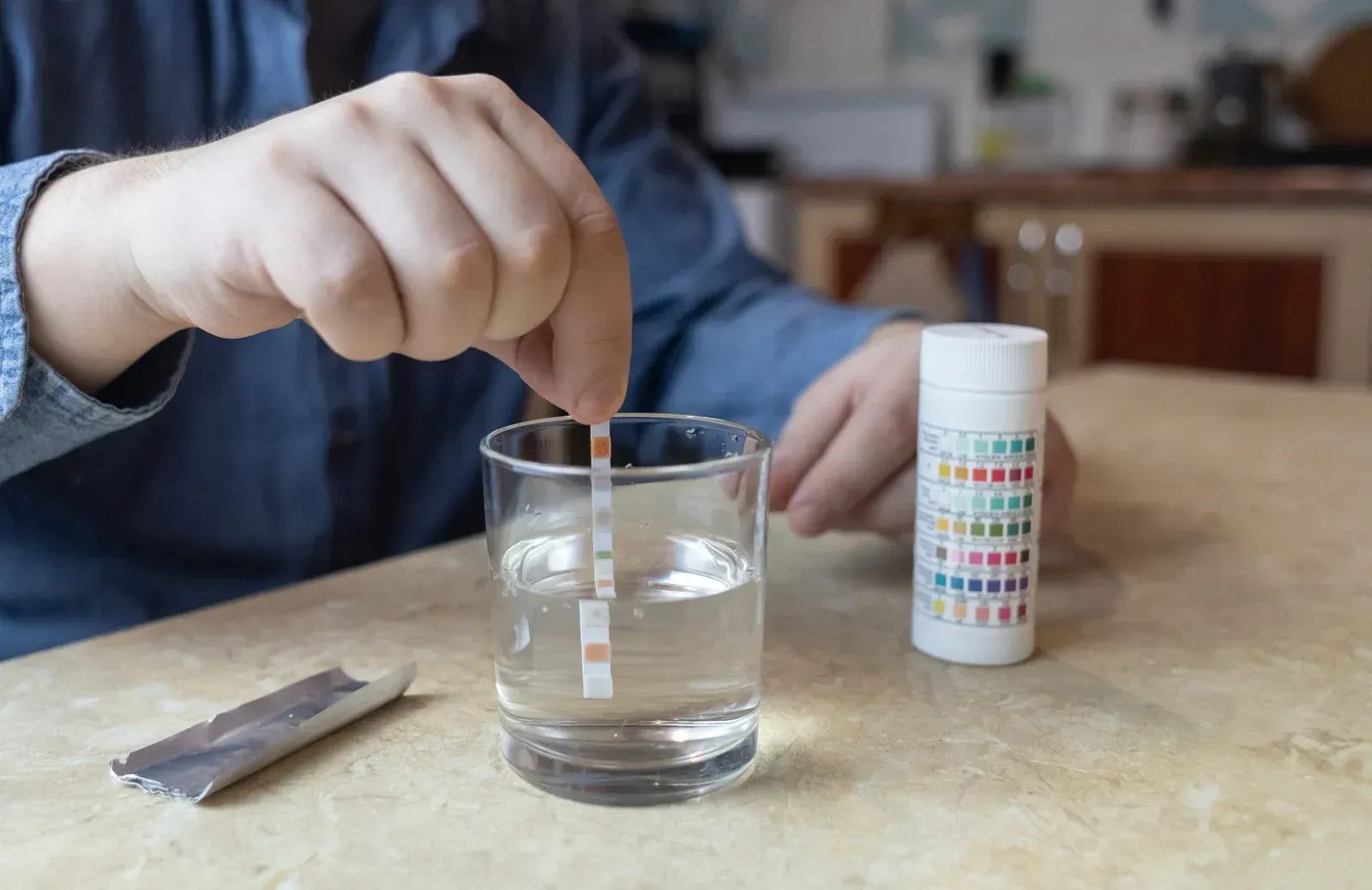Hand placing a test strip into a glass of water beside a pH test kit on a table