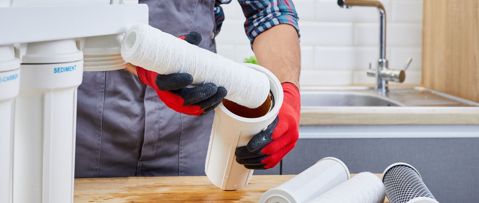 Person in red gloves installing a white pipe under a kitchen sink with tools nearby