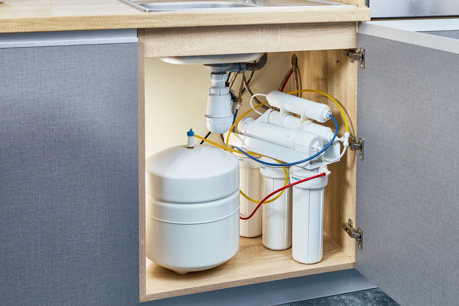 Under-sink water filtration system with white tanks and tubing inside a cabinet