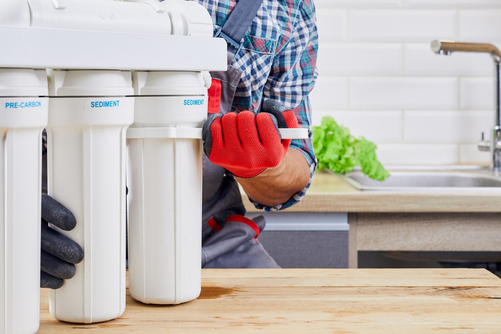 Person installing a white under-sink water filter in a kitchen, wearing red gloves