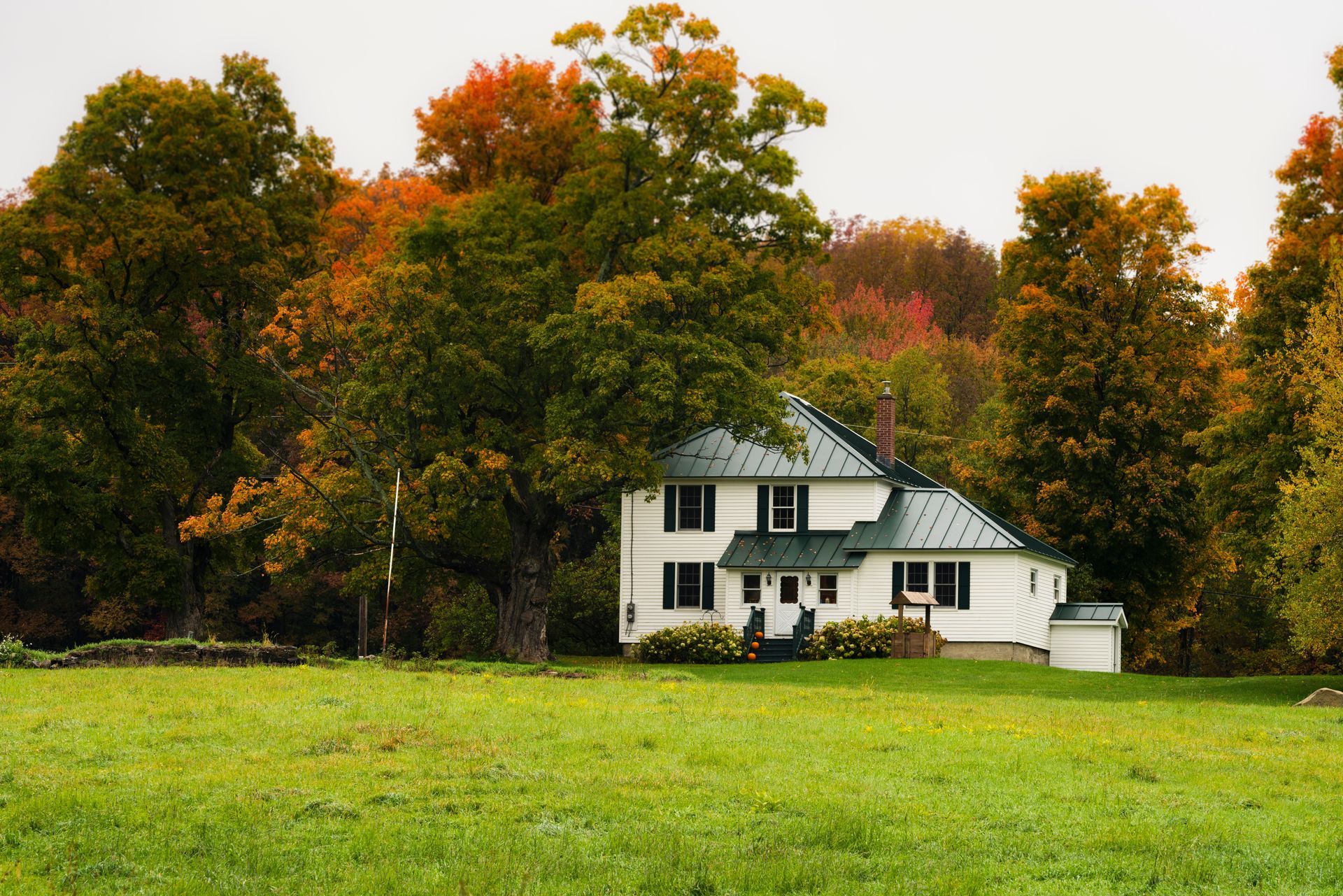 White house with green roof amidst colorful autumn trees in a grassy field. White house with green roof amidst colorful autumn trees in a grassy field.