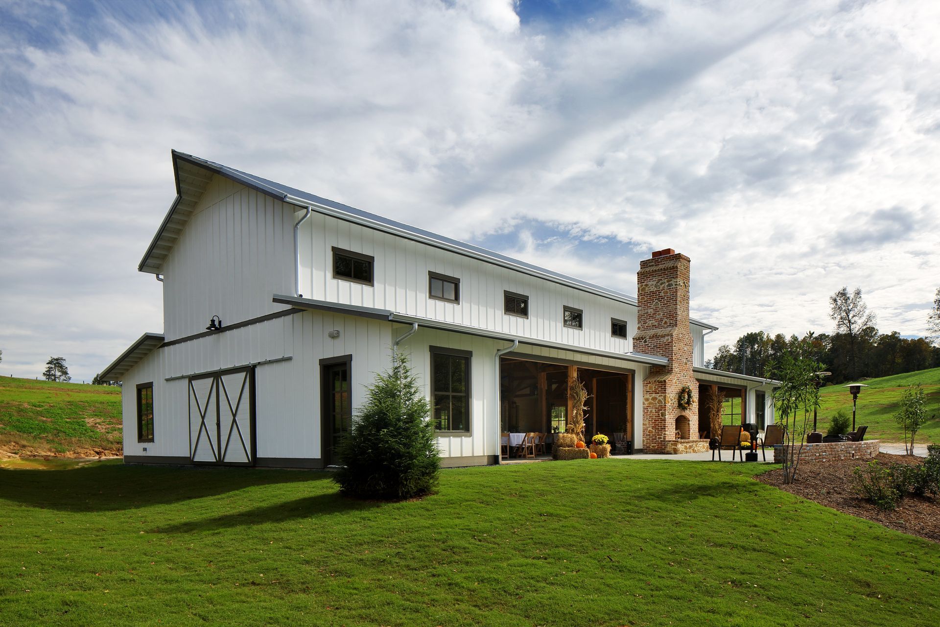 White barn with a gray roof and stone chimney on a grassy hill under a partly cloudy sky. White barn with a gray roof and stone chimney on a grassy hill under a partly cloudy sky.