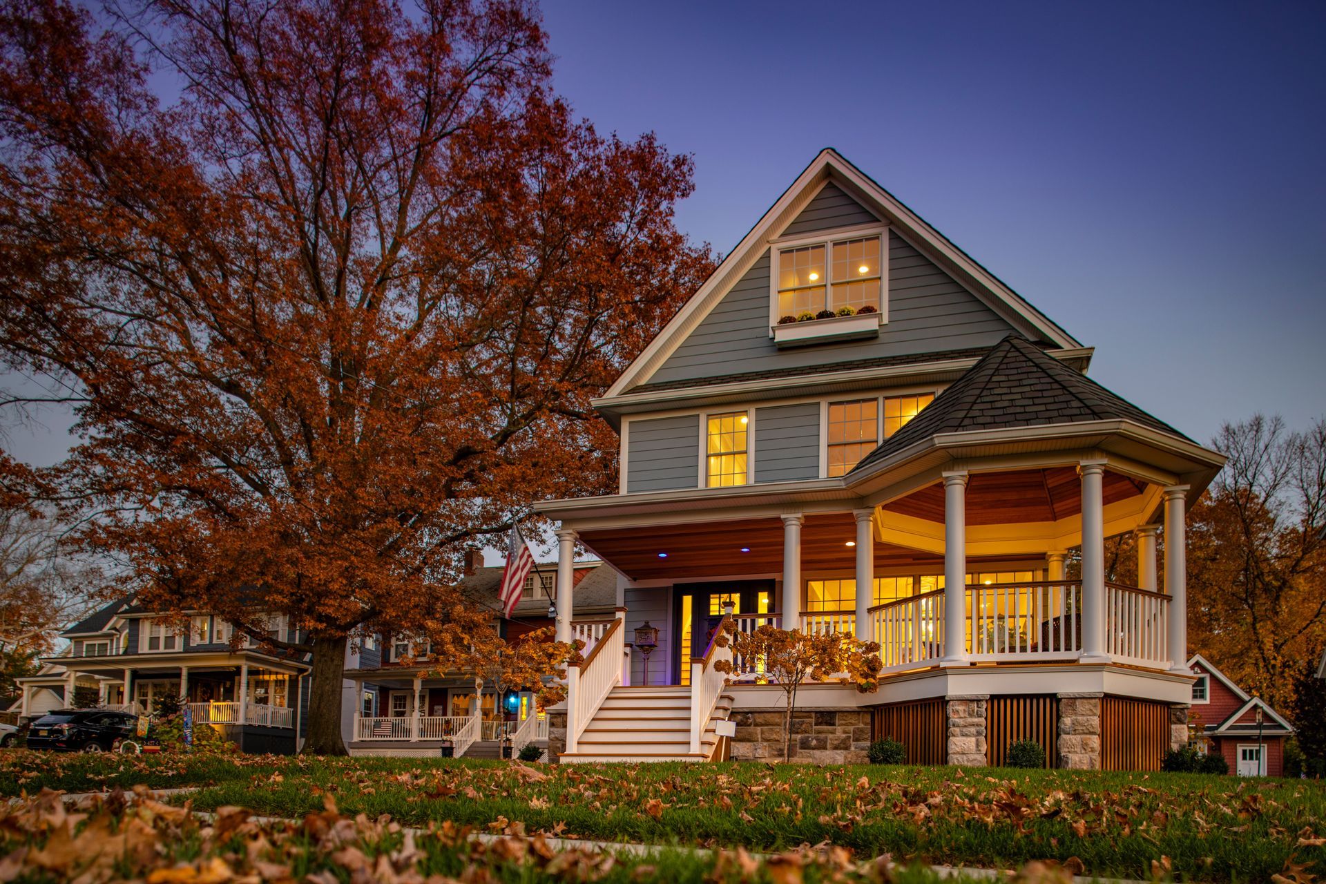 Two-story house with a porch and fall foliage, lit from within, at dusk. Two-story house with a porch and fall foliage, lit from within, at dusk.