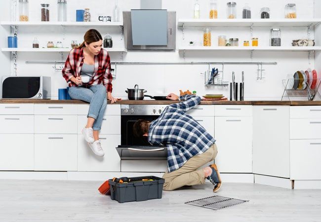 Young Woman Watching a Handyman Repairing an Oven — Dalzell, SC — Dalzell Appliance Parts Service & Sales Young Woman Watching a Handyman Repairing an Oven — Dalzell, SC — Dalzell Appliance Parts Service & Sales