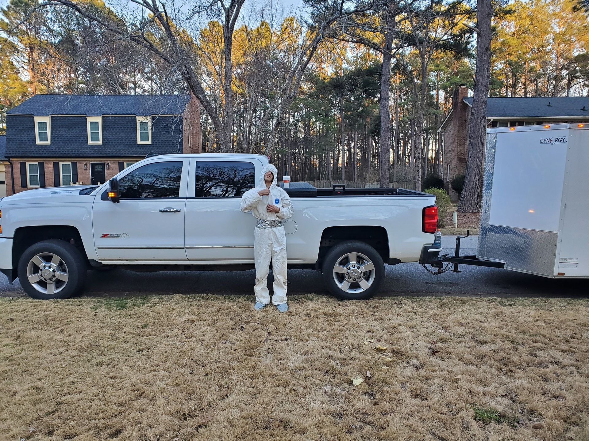 A man in a white suit is standing next to a white truck and trailer.