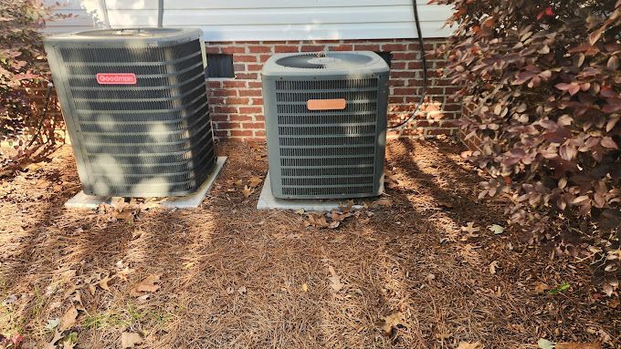 Two air conditioners are sitting next to each other in front of a brick building.