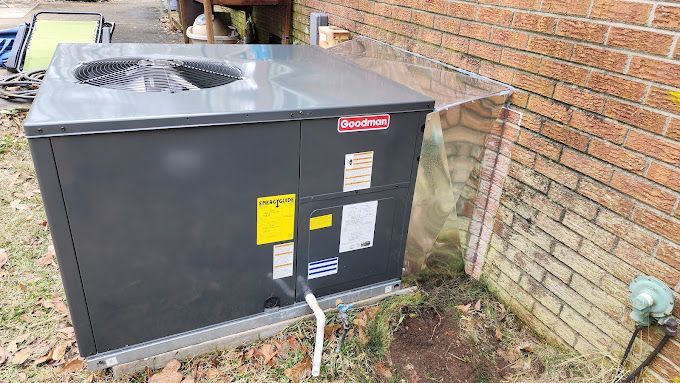 A black air conditioner is sitting next to a brick wall.